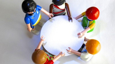 Bunte Spielfiguren sitzen im Kreis um einen großen aufblasbaren Ball.
