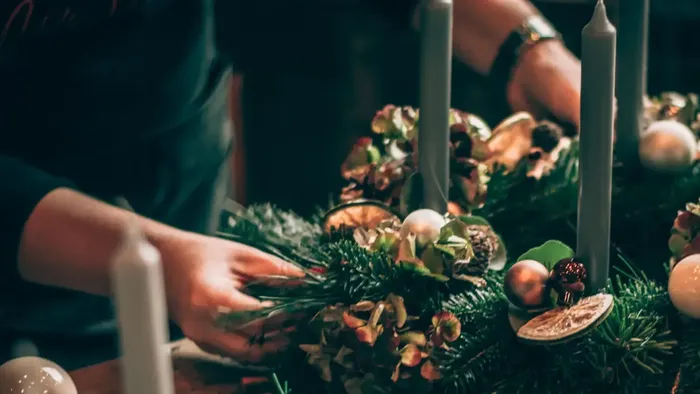 Eine Person dekoriert einen Weihnachtsstrauß mit Tannenzapfen und Kugeln.