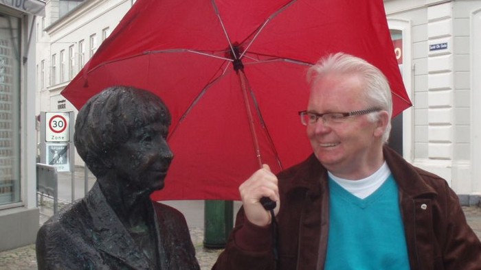 Mand med rød paraply står ved statue.