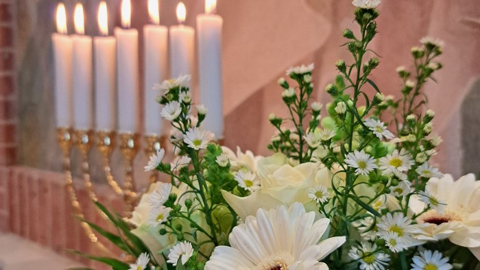 Elegant blomsterarrangement med hvide blomster og grønt ved siden af tændte lys på et bord.