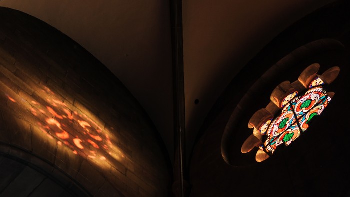 Fenêtre en vitrail vibrant représentant des motifs floraux ou géométriques colorés, illuminée sur un fond sombre.