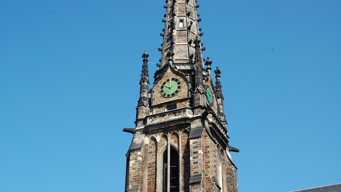Der Kirchturm mit Uhr und Kreuz vor blauem Himmel