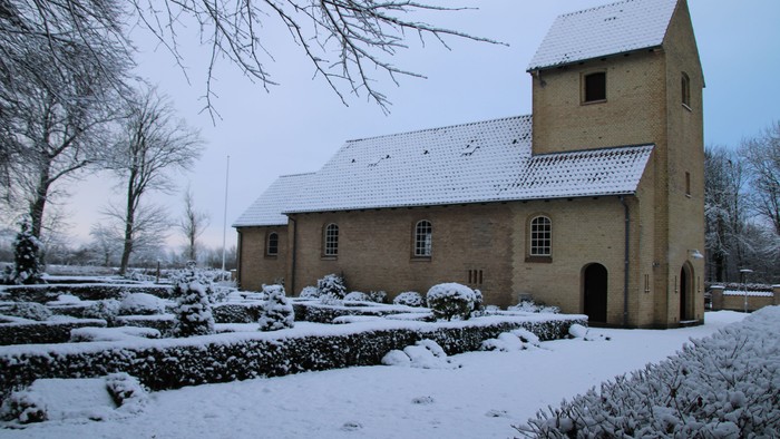 En snedækket kirke med tårn og rund vindueskarm i en snedækket have