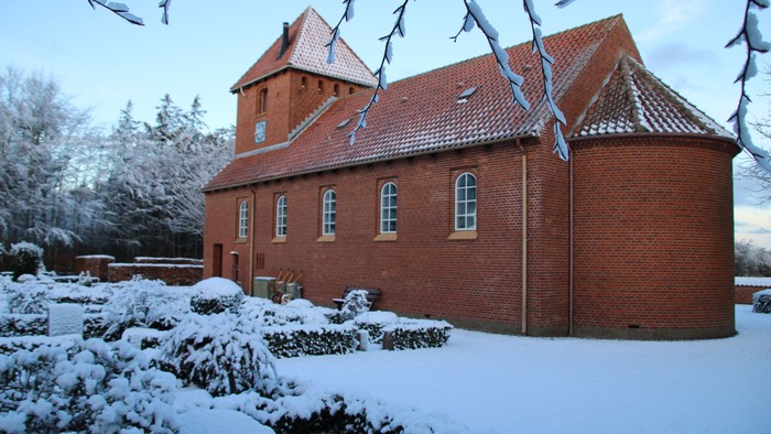 Røde murstenskirke med spiret og tage i sneklædt landskab