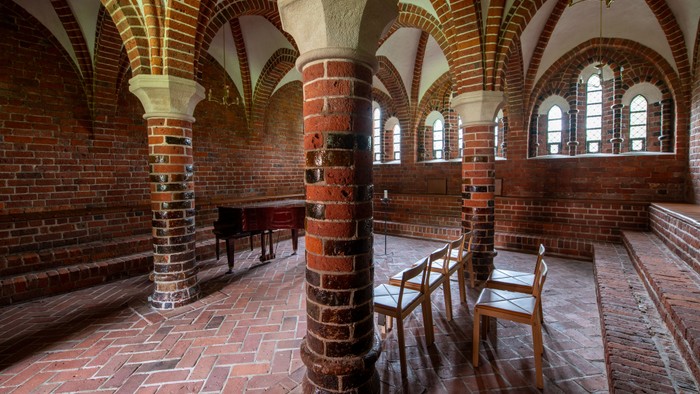 Historisk murstenshal med hvælvede lofter, træbænke og flisegulve.