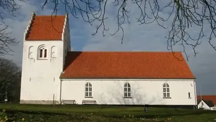 Hyggelig hvid kirke med rødt tegltag indlejret i et fredfyldt, grønt landskab.
