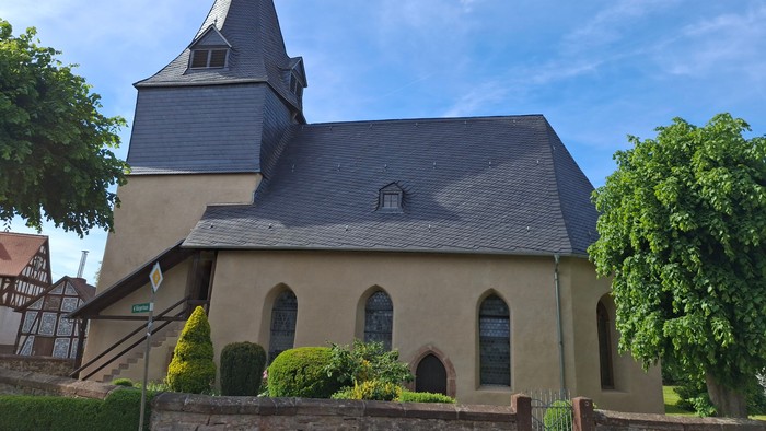 Idyllische Kirche mit steilem Dach, Bogenfenstern und üppigem Grün drumherum.