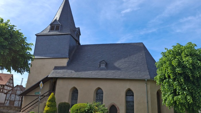 Idyllische Kirche mit steilem Dach, Bogenfenstern und üppigem Grün drumherum.