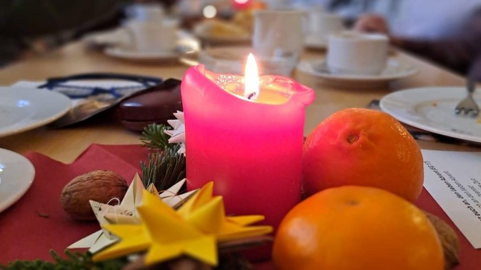 Tisch gedeckt mit Kerze, Orangen und Grünzeug; Personen im Hintergrund.