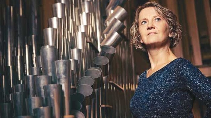 En kvinde står ved siden af et stort, indviklet musikinstrument, der ligner et klokkespil eller rørklokker.