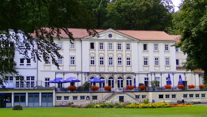 Elegantes weißes Gebäude mit Blumenkästen, blauen Sonnenschirmen und üppiger grüner Umgebung.