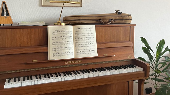 Elegantes Holzklavier mit Notenblättern, gerahmten Kunstwerken und einer kleinen Topfpflanze in der Nähe.