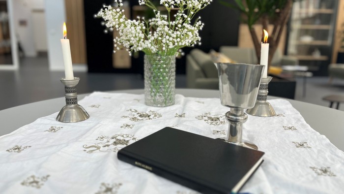Elegant borddækning med stearinlys, blomstervase, bæger, notesbog og pen på en dekoreret dug.