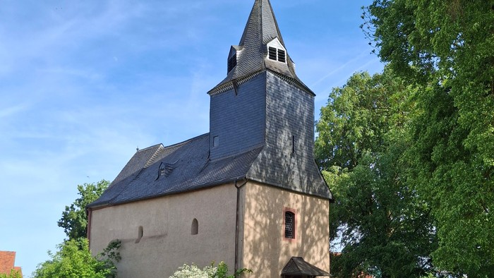 Historische Steinkirche mit hohem Glockenturm, umgeben von üppigem Grün und einem Kopfsteinpflasterweg.