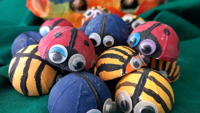 Bunte handgefertigte Ballfiguren mit Wackelaugen und bemalten Streifen auf grünem Stoffhintergrund.