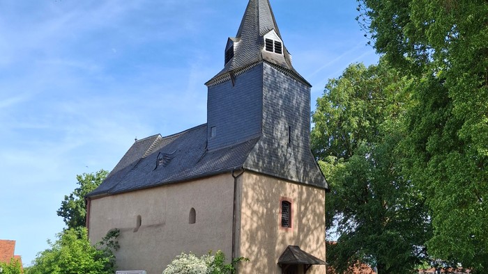Historische Steinkirche mit hohem Glockenturm, umgeben von üppigem Grün und einem Kopfsteinpflasterweg.