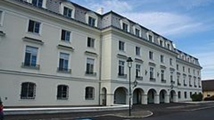 Großes, weißes Gebäude mit vielen Fenstern und Bögen an der Straße.