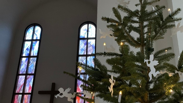 En juletree med stjerner og lys foran et vindueskarm med glasmalerier