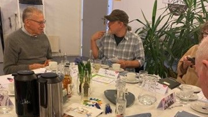 En gruppe mennesker sidder ved et bord med kage og teetøj.