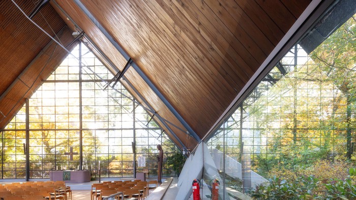 Moderner Innenraum mit Holzdecke, großen Glaswänden und natürlichem Licht, das die grüne Umgebung draußen sichtbar macht.