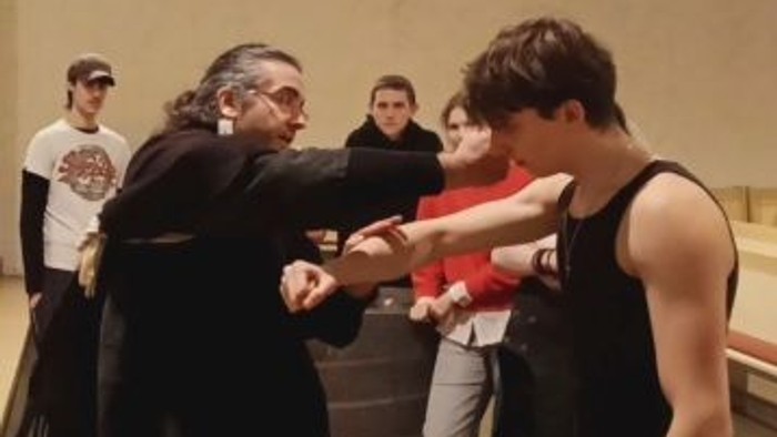 Zwei Männer üben Kampfsport-Handtechniken, während andere in einer Trainingseinheit zusehen.