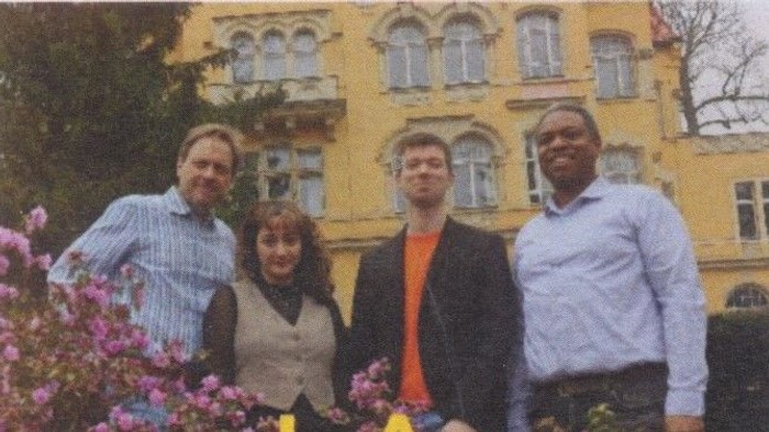 Vier Personen stehen vor einem gelben Gebäude mit Blumen.