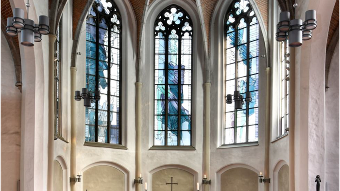 Elegante Kircheninnenausstattung mit hohen Buntglasfenstern, hölzernen Kirchenbänken und einem zentralen Altar mit einem Kreuz.