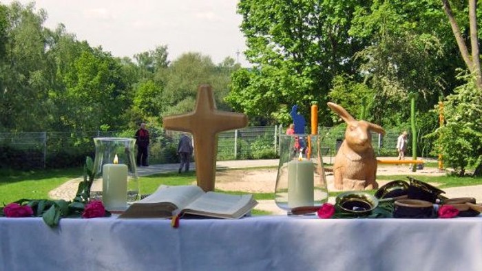 Aufbau eines Outdoor-Altars mit religiösen Gegenständen, Kerzen, Büchern und einer kleinen Hasenfigur auf einem Tisch.