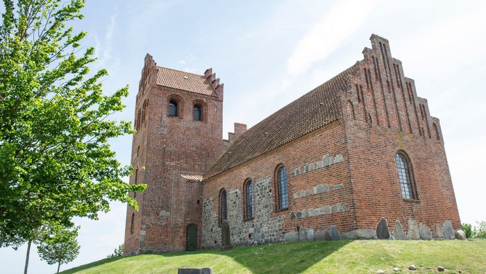Ruinen af en gammel kirke på en grøn bakke under et klart blå himmel.