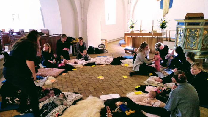 Gruppe, der mediterer eller slapper af i en kirke med måtter og tæpper arrangeret på gulvet.