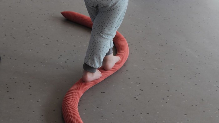 Ein Kind tritt auf eine große, rote, schlangenförmige Spielmatte.