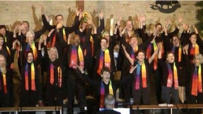Eine Gruppe von Menschen in schwarzen Roben und farbenfrohen Tüchern feiert auf einer Bühne.