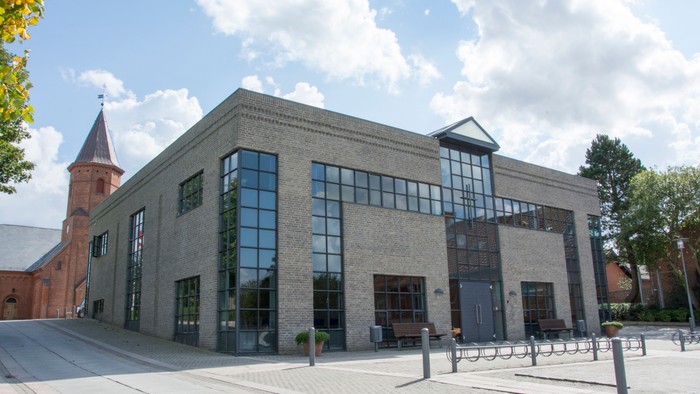 Et moderne bygning med store vinduer og en kirke med tårn ved siden af