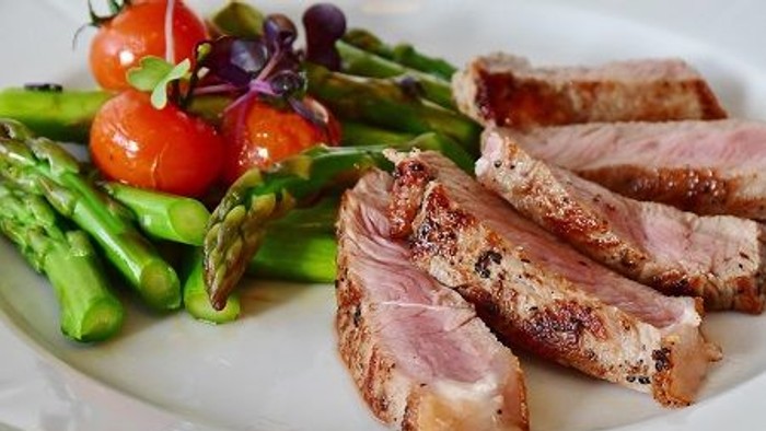 Das Bild zeigt ein Gericht mit gegrilltem Fleisch, Spargel und Tomaten