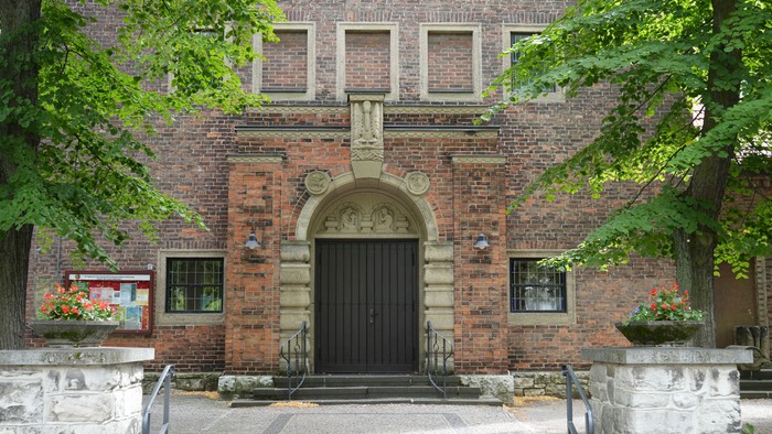 Historischer Ziegelsteingebäude-Eingang, eingerahmt von Grünpflanzen und Steintreppen.