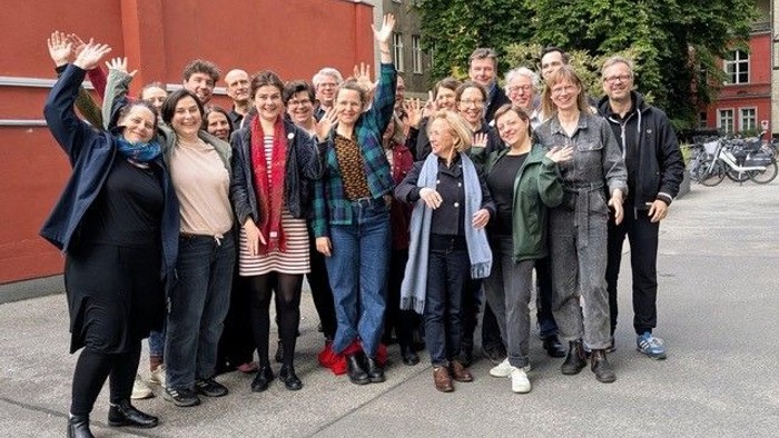Eine fröhliche Gruppe von Menschen, die draußen gemeinsam posieren, mit erhobenen Händen und lächelnden Gesichtern.