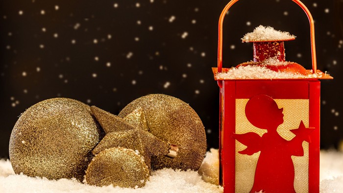 Winterszene mit einer schneebedeckten roten Laterne, umgeben von glitzernden goldenen Ornamenten vor einem verschneiten Hintergrund.