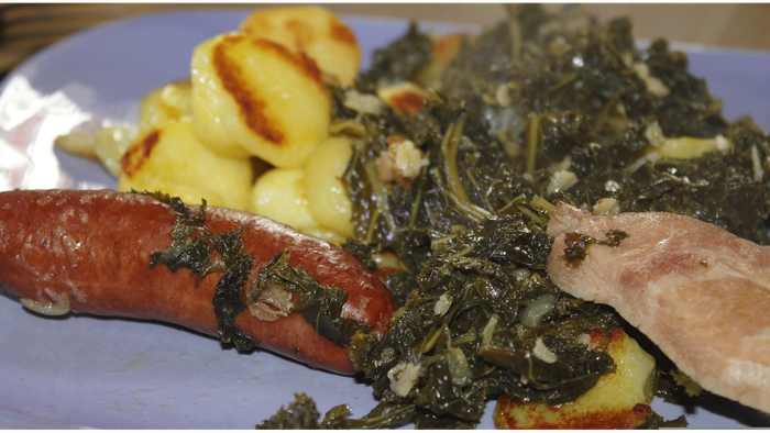 Ein herzhaftes Gericht mit gegrillter Wurst, Grünkohl, Kartoffelpüree und Speck.