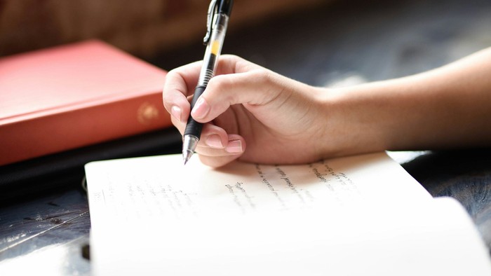 Hand schreibt mit Kugelschreiber auf Papier