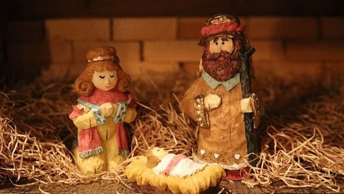Drei Holzfiguren in Krippe, Mann mit Bart und Hut, Frau mit Kleid, Baby im Korb.