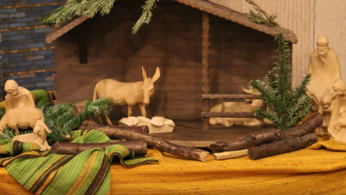 Eine Krippe mit Holzfiguren und Tannengrün, ein Esel steht vor der Krippe.