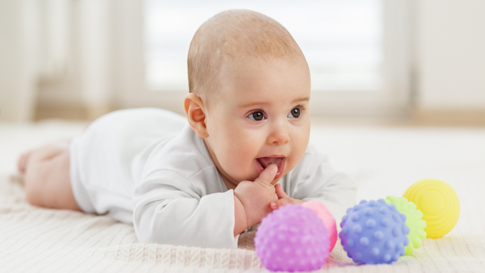 Süßes Baby spielt mit bunten, strukturierten Babyspielzeugen auf einer weichen Unterlage.