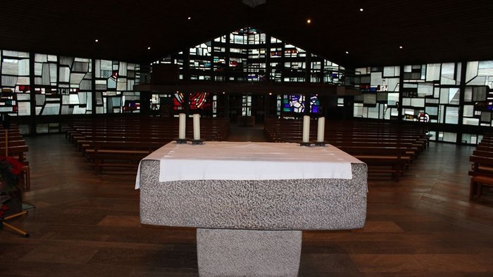 Ein moderner Altar in einer großen, dunklen Kirche mit vielen Fenstern.