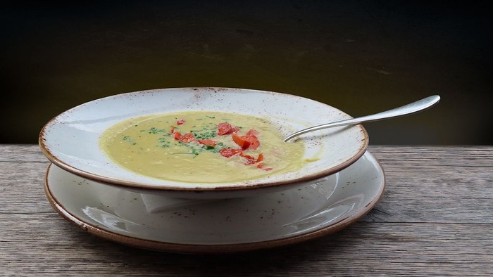 En bolle med grøn suppe og tomater på en hvid tælle under en skovl