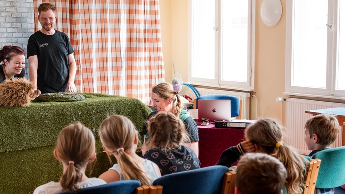 Mehrere Kinder sitzen auf Stühle un schauen einem Puppentheater zu