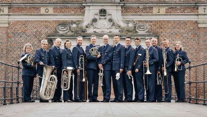 En gruppe musikere i blå uniformer stående med messinginstrumenter foran Kronborg Slot