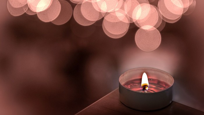 Eine kleine brennende Kerze auf einer Oberfläche mit weichen, unscharfen Bokeh-Lichtern im Hintergrund.