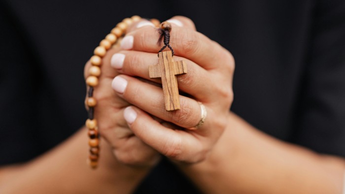 Hände halten Holzkreuz und Rosenkranz