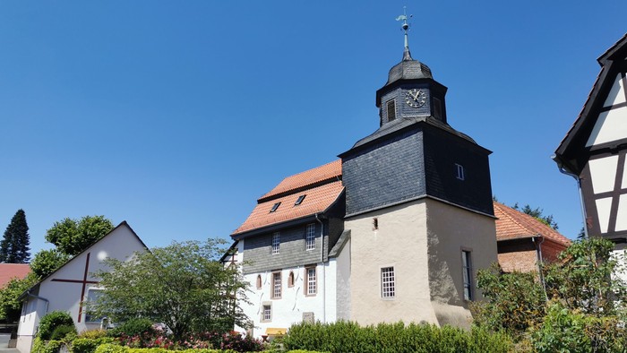 Ein weißes Gebäude mit schwarzem Dach und Uhrturm, umgeben von grünen Büschen und Bäumen