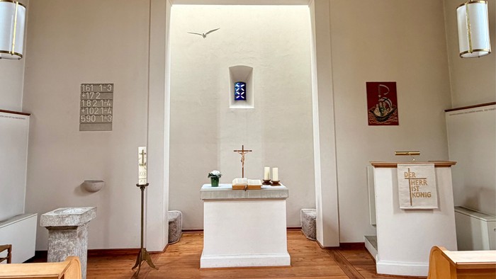 Ein ruhiger Kapelleninnenraum mit einem Altar, auf dem Kerzen stehen, einem Kreuz und religiösen Symbolen an den Wänden.